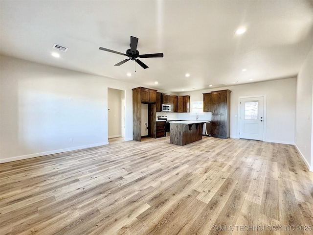 kitchen with a kitchen island, visible vents, open floor plan, light wood finished floors, and stainless steel microwave