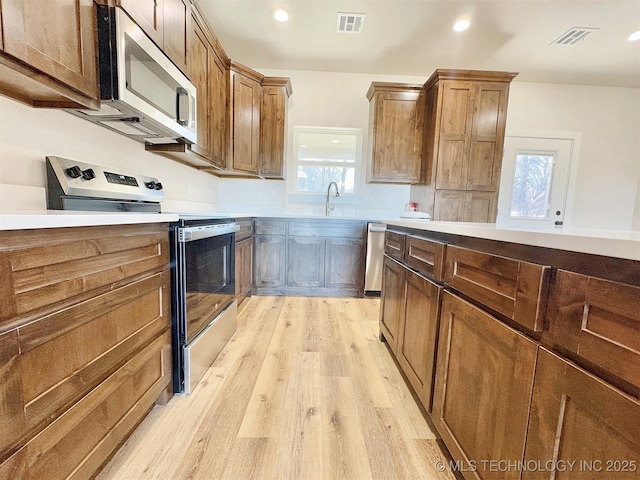 kitchen with a sink, visible vents, light wood-style floors, light countertops, and appliances with stainless steel finishes