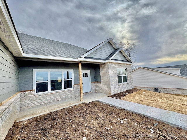 property entrance featuring a shingled roof and brick siding