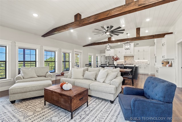 living room featuring ceiling fan with notable chandelier, a healthy amount of sunlight, light hardwood / wood-style floors, and lofted ceiling with beams