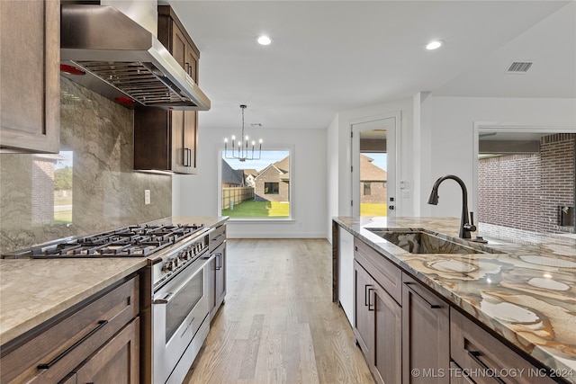 kitchen featuring pendant lighting, sink, wall chimney exhaust hood, light wood-type flooring, and stainless steel range