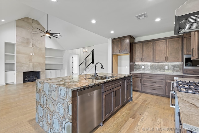 kitchen featuring sink, vaulted ceiling, an island with sink, stainless steel appliances, and a tiled fireplace