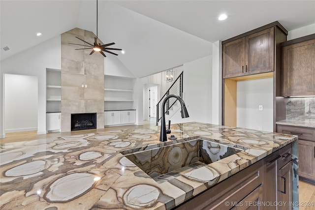 kitchen featuring light stone countertops, light wood-type flooring, built in shelves, ceiling fan, and a fireplace