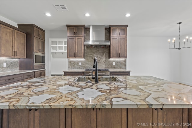 kitchen featuring a notable chandelier, decorative backsplash, a spacious island, and wall chimney range hood