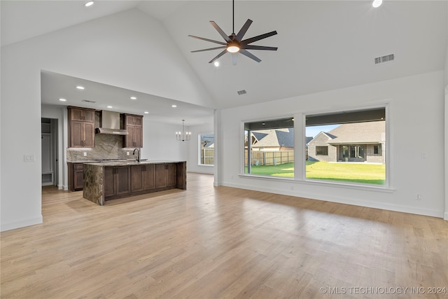 unfurnished living room with ceiling fan with notable chandelier, light hardwood / wood-style flooring, high vaulted ceiling, and sink