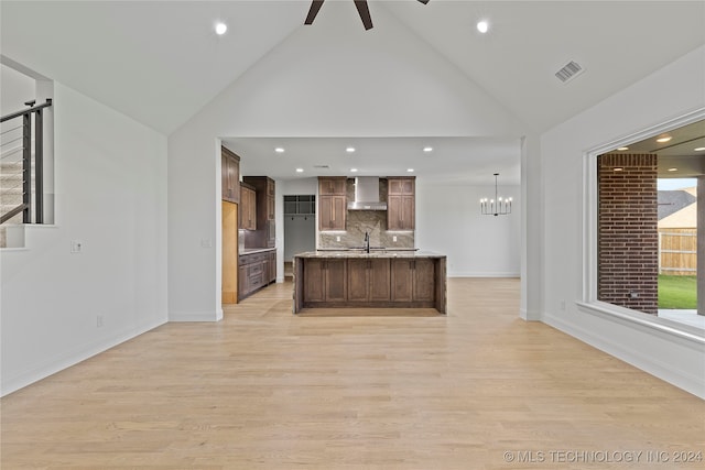 kitchen with pendant lighting, wall chimney range hood, sink, light hardwood / wood-style flooring, and decorative backsplash