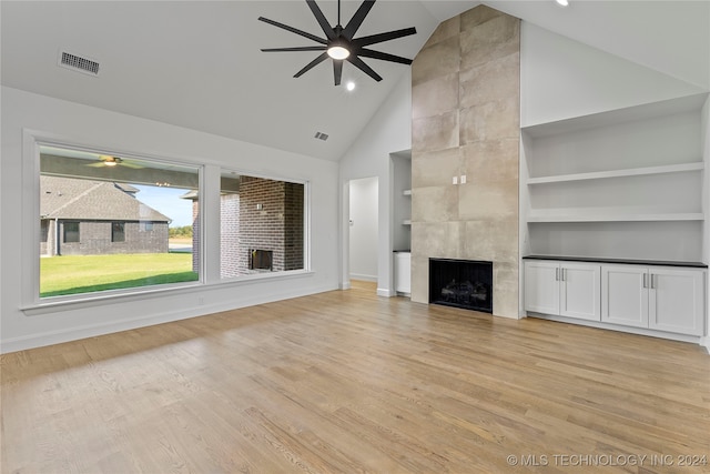 unfurnished living room featuring a tile fireplace, ceiling fan, built in features, and light hardwood / wood-style flooring