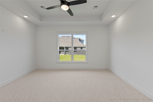 carpeted spare room with a raised ceiling and ceiling fan