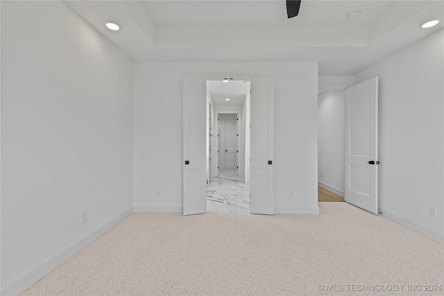 unfurnished bedroom featuring a tray ceiling, ceiling fan, and light colored carpet