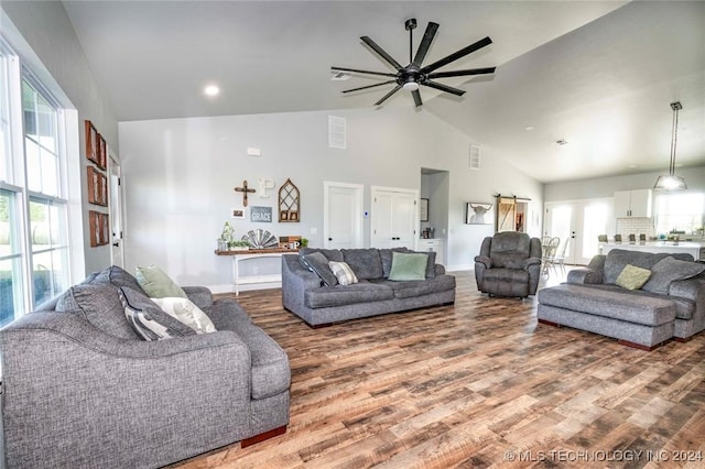 living room with high vaulted ceiling, ceiling fan, hardwood / wood-style floors, and a barn door