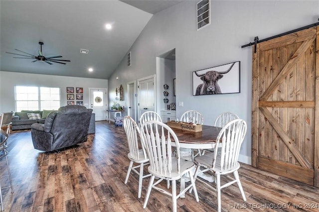 dining space with ceiling fan, hardwood / wood-style floors, a barn door, and high vaulted ceiling