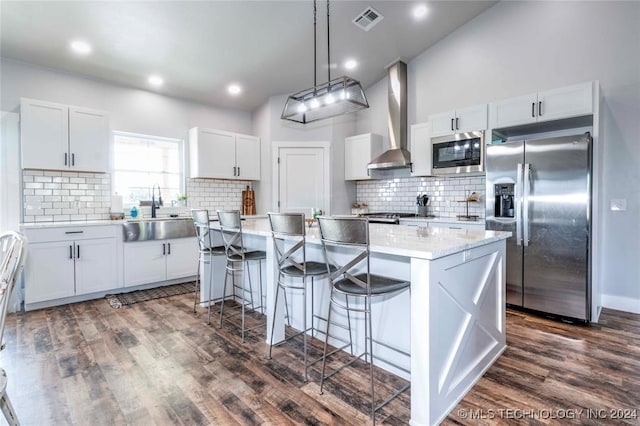 kitchen with white cabinets, sink, wall chimney exhaust hood, appliances with stainless steel finishes, and a center island