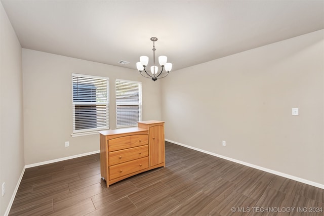 unfurnished dining area with dark wood-type flooring and an inviting chandelier