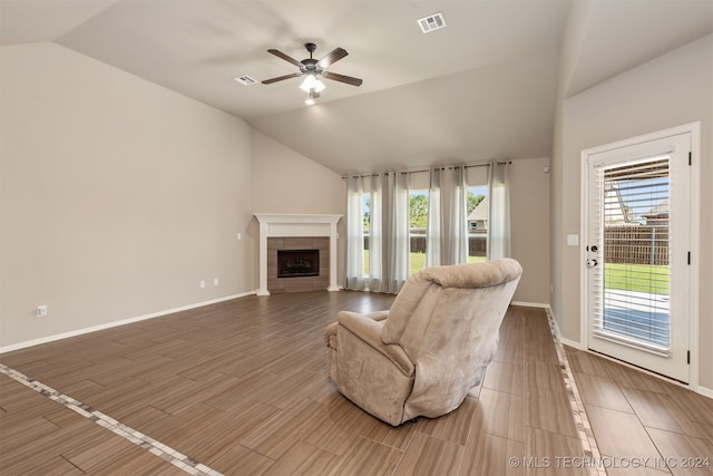 living room featuring hardwood / wood-style flooring, lofted ceiling, a tiled fireplace, and a healthy amount of sunlight