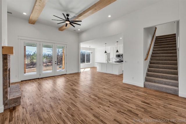 unfurnished living room featuring sink, ceiling fan with notable chandelier, beam ceiling, hardwood / wood-style floors, and french doors