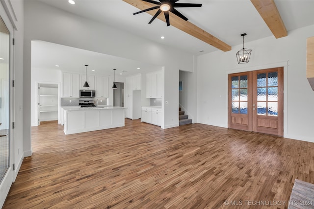 unfurnished living room with french doors, ceiling fan with notable chandelier, light wood-type flooring, and beam ceiling