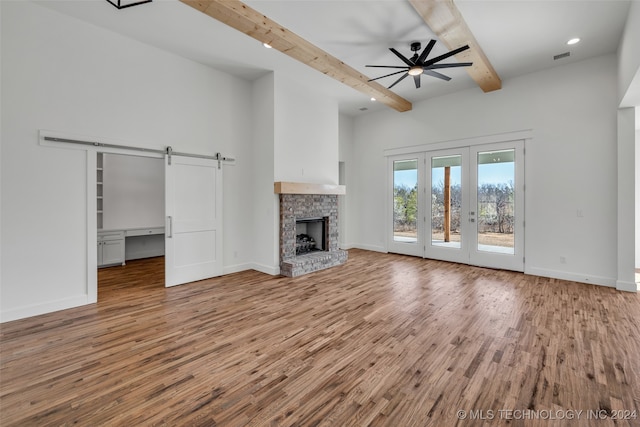 unfurnished living room with a barn door, a fireplace, beamed ceiling, ceiling fan, and hardwood / wood-style flooring