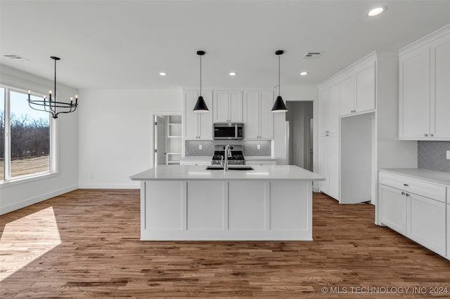 kitchen with appliances with stainless steel finishes, white cabinetry, an island with sink, and hardwood / wood-style flooring