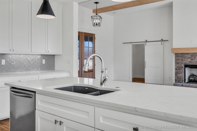 kitchen with white cabinetry, a barn door, decorative light fixtures, stainless steel dishwasher, and sink