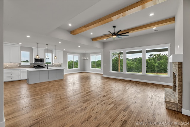 unfurnished living room with sink, beam ceiling, a fireplace, ceiling fan with notable chandelier, and light hardwood / wood-style floors