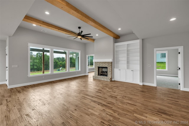 unfurnished living room featuring a brick fireplace, beamed ceiling, hardwood / wood-style flooring, and a wealth of natural light