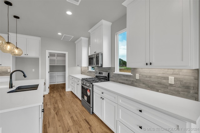 kitchen featuring pendant lighting, light hardwood / wood-style floors, sink, white cabinetry, and appliances with stainless steel finishes