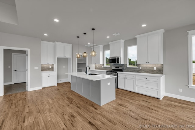 kitchen with hanging light fixtures, sink, a center island with sink, white cabinetry, and appliances with stainless steel finishes