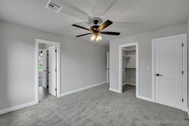 unfurnished bedroom featuring a walk in closet, ceiling fan, light colored carpet, and a closet