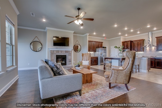 living room featuring ornamental molding, ceiling fan, a brick fireplace, and hardwood / wood-style flooring