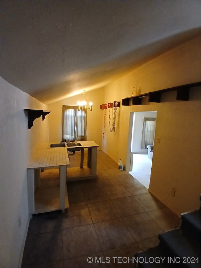 corridor with dark tile patterned flooring, a chandelier, and vaulted ceiling