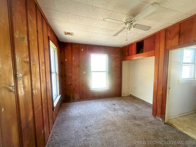 unfurnished bedroom with ceiling fan, wooden walls, and carpet