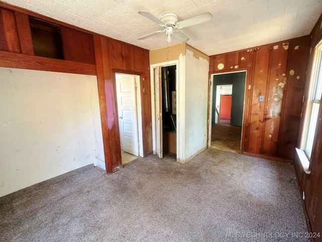 unfurnished bedroom with wooden walls, carpet flooring, and ceiling fan