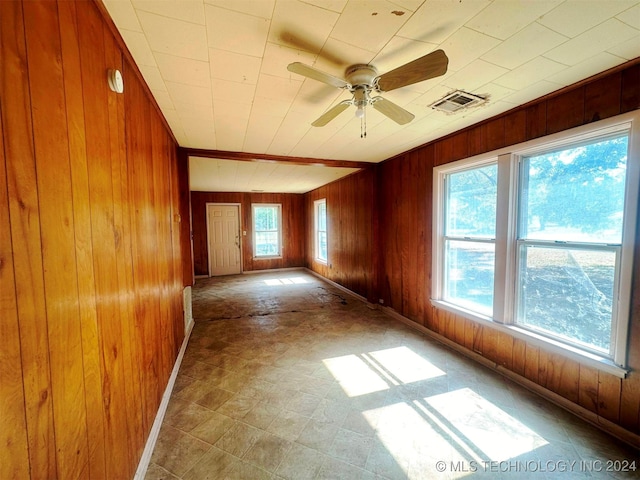 unfurnished room with wood walls, a wealth of natural light, vaulted ceiling, and ceiling fan