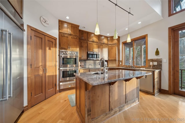 kitchen with a sink, appliances with stainless steel finishes, backsplash, brown cabinets, and a warming drawer