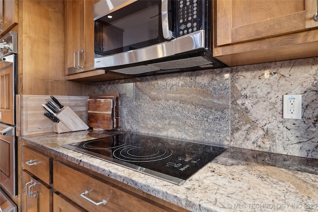 kitchen with brown cabinets, stainless steel microwave, decorative backsplash, and black electric stovetop