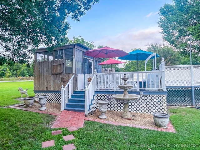 rear view of property featuring a deck, a sunroom, and a lawn