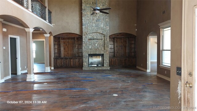 unfurnished living room featuring a high ceiling, decorative columns, a healthy amount of sunlight, and dark wood-type flooring