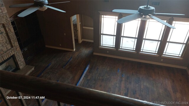 unfurnished living room featuring dark wood-type flooring, ceiling fan, and a stone fireplace