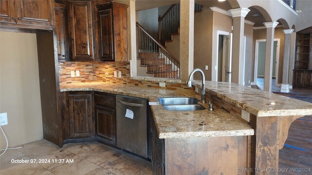 kitchen with light stone counters, sink, kitchen peninsula, stainless steel dishwasher, and a kitchen bar