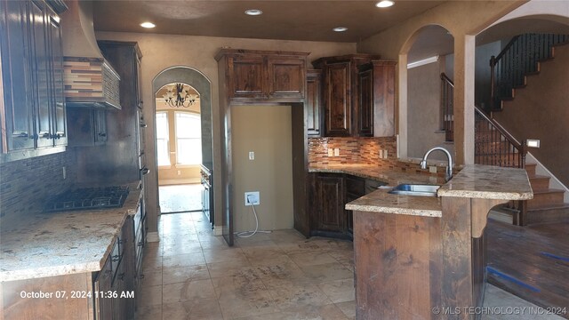 kitchen featuring light stone counters, dark brown cabinets, exhaust hood, and sink