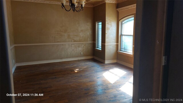 spare room with a notable chandelier, crown molding, and dark wood-type flooring