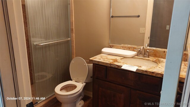 bathroom with hardwood / wood-style flooring, a shower with shower door, vanity, and toilet