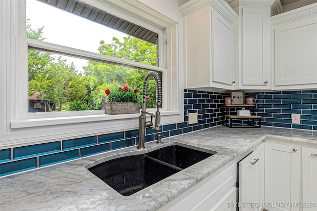 kitchen with light stone counters, decorative backsplash, white cabinetry, and sink