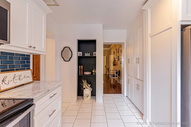 kitchen featuring light stone countertops, decorative backsplash, white cabinetry, and light tile patterned floors