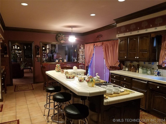 kitchen featuring crown molding, a kitchen island, dark brown cabinetry, and tile counters