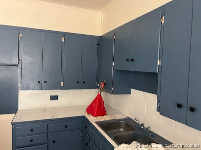 kitchen with blue cabinetry, ornamental molding, backsplash, and sink