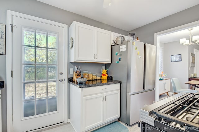 kitchen with white cabinets, stainless steel fridge, hanging light fixtures, and dark stone counters