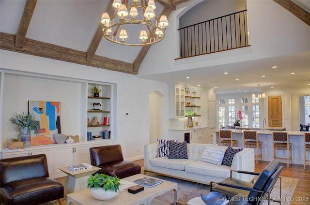 living room with high vaulted ceiling, wood-type flooring, a chandelier, beam ceiling, and built in shelves