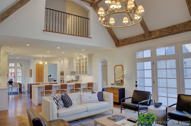 living room with beam ceiling, a high ceiling, a chandelier, and light hardwood / wood-style flooring