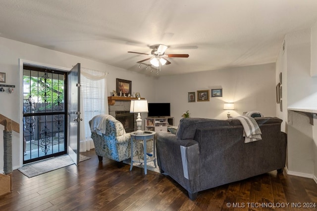 living room featuring ceiling fan, a stone fireplace, and dark hardwood / wood-style floors